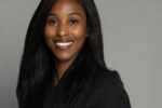 Nancy Williams is smiling warmly at the camera. She has long, straight black hair and is dressed in a black blazer over a dark top.
