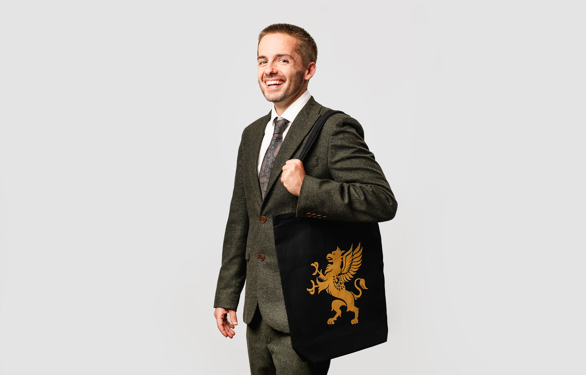 Model wearing a suit with black tote bag with gold logo, on white background