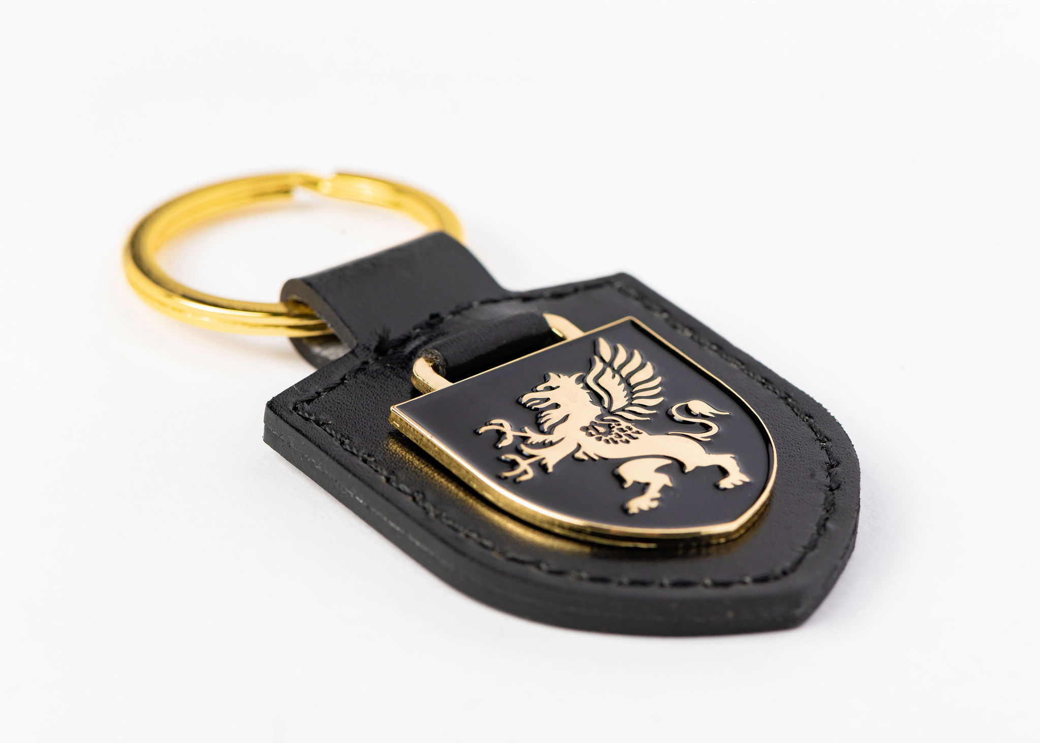 Shield keyring in black faux leather with gold enamel griffin laid flat on a white background
