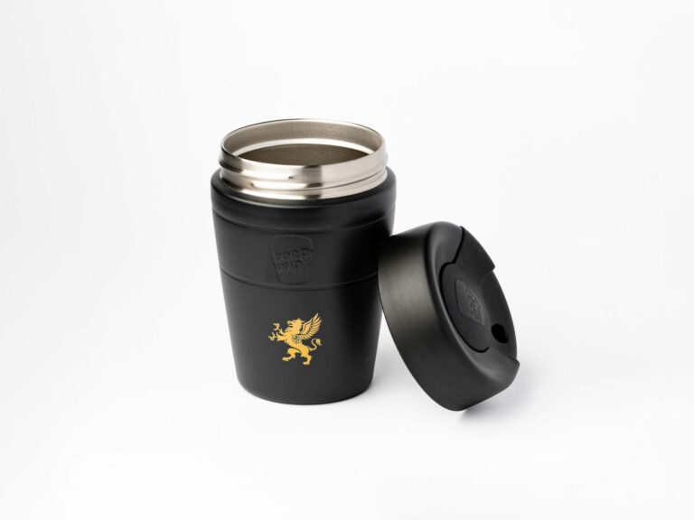 A sleek, black insulated travel mug with a metallic interior is shown against a white background. The lid is off and placed to the side, revealing the mug's opening. A gold emblem of a griffin is prominently displayed on the front of the mug. The brand name "KeepCup" is subtly embossed on the side.