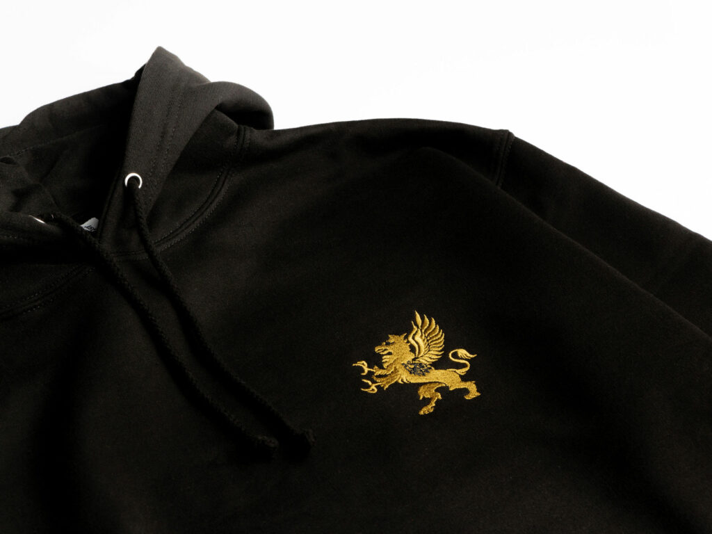 A black hoodie is displayed against a plain white background. The hoodie features a gold emblem of a griffin embroidered on the chest area