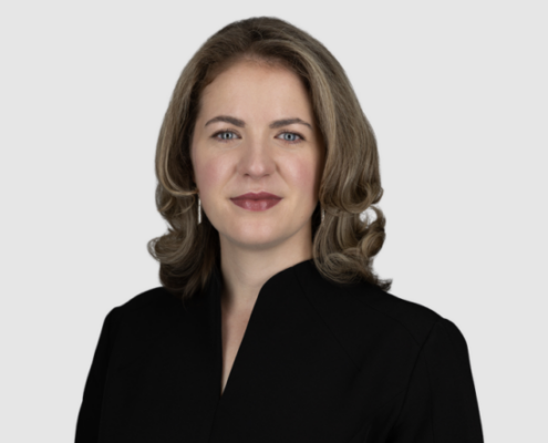 A professional headshot of Charlotte Branfield on a plain white background, who is dressed in a black blazer. Her hair is styled in soft waves, and she has a confident expression.