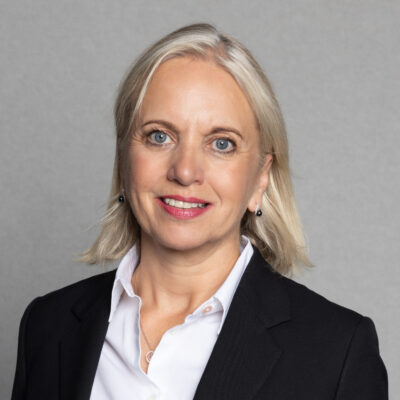 Headshot of Kirsty Brimelow, who is dressed in a black blazer over a white collared shirt. She has short blonde hair and is wearing small earrings.