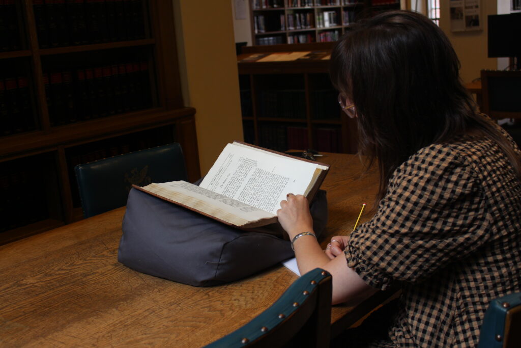 User looking through a special collection book carefully supported on a conservation cushion in the Library.