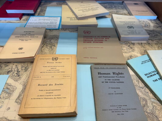 A display of United Nations publications arranged on a map-patterned surface. Visible titles include “Treaty Series” in English and French, “Judgements of the United Nations Administrative Tribunal,” “Proceedings of the Seminar on Petroleum Legislation with Particular Reference to Offshore Operations,” “Human Rights and Fundamental Freedoms in the Charter of the United Nations,” and “Selected Human Rights Documents.” The booklets are in muted tones and date from the mid twentieth century.