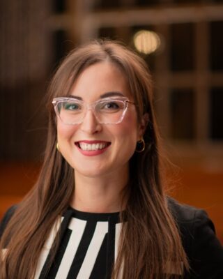 Portrait photograph og Member Angharad Hughes, wearing glasses with a side fringe, and black and white striped top